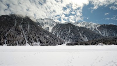 Der Antholzer See wird von dunklen Wäldern und majestätischen Gipfeln umrahmt