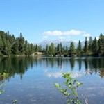 Der Puntleider See wird von Bäumen und den dahinter aufragenden Bergspitzen umrahmt